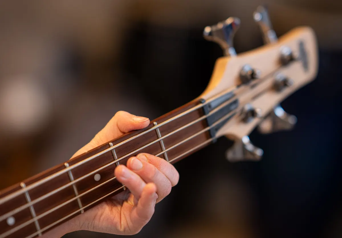 A hand fretting a note on the neck of a bass guitar