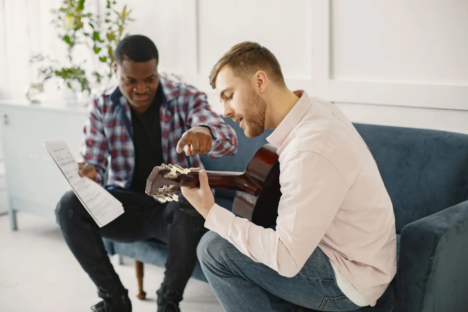 A teacher pointing out a chord to an adult guitar student on a sofa